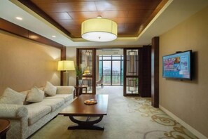 A hotel lobby with a sofa, a table with a plate of pastries, a television on the wall, and a view through a glass door to the outside.