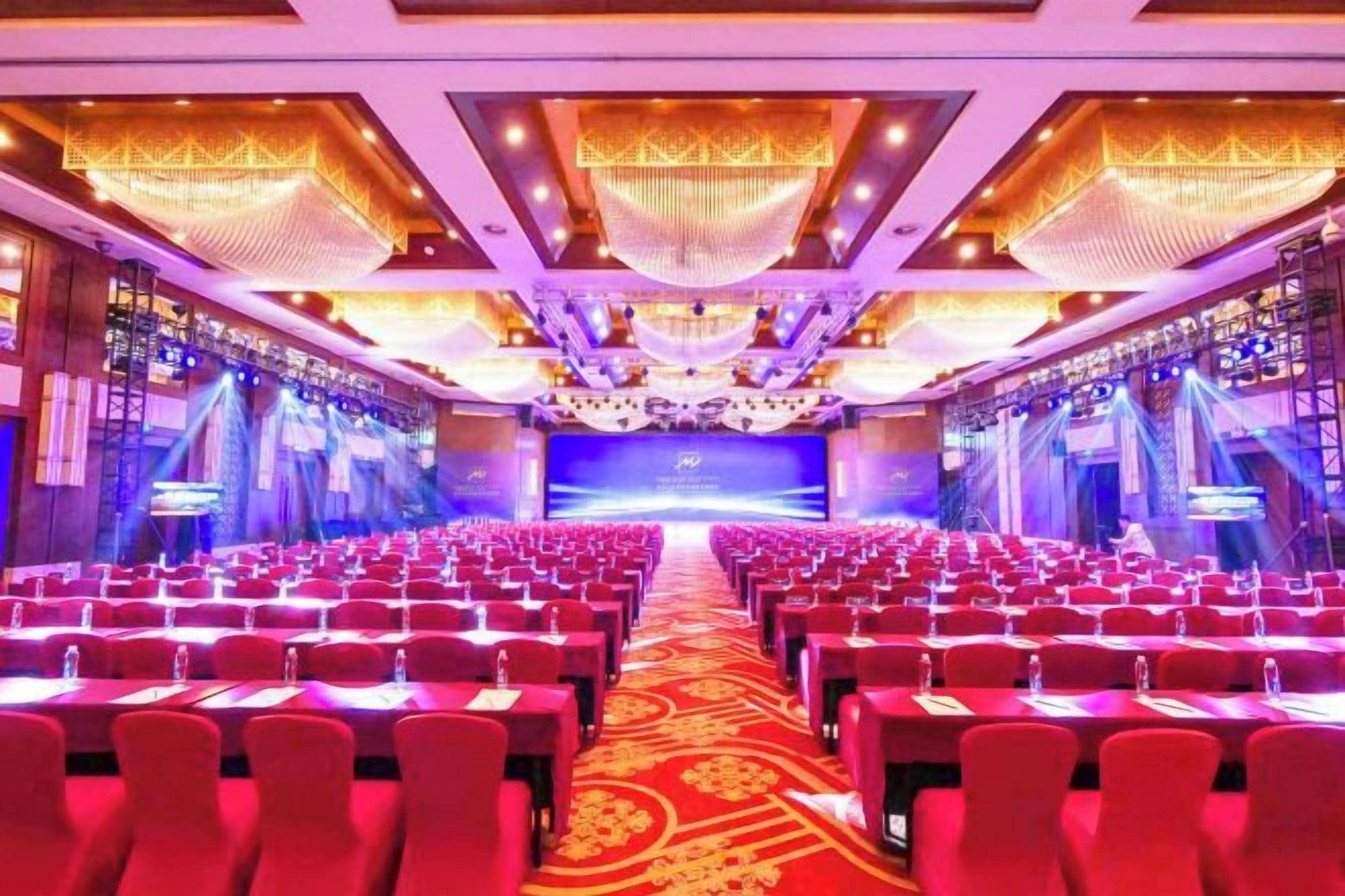 A conference room with rows of tables and chairs, a stage at the front, and a large screen.