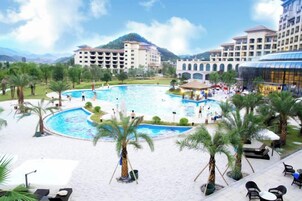 Un resort con piscina central, palmeras y montañas al fondo.
