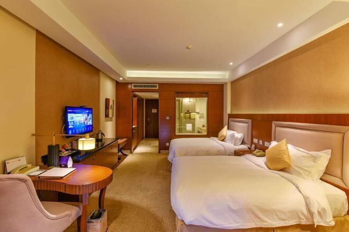 A hotel room with two beds, a desk with a computer, a television, and a bathroom visible through an open door.