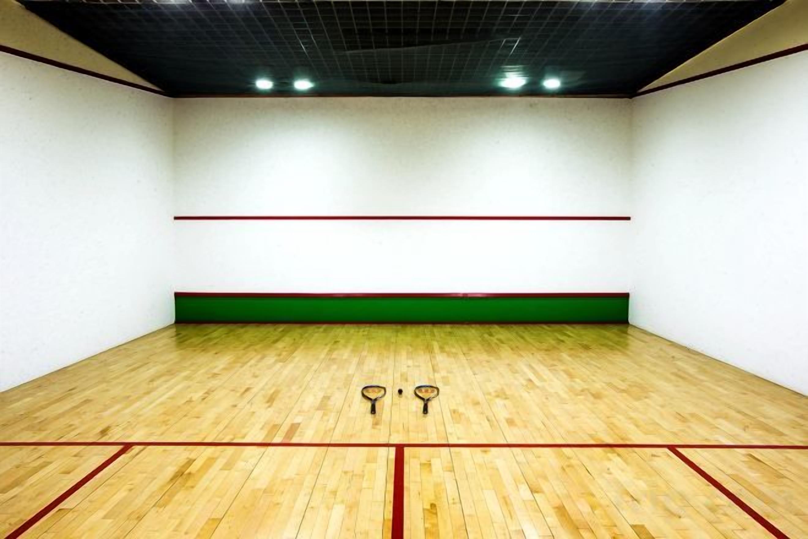 A squash court with a wooden floor, green and red lines, and two squash rackets.