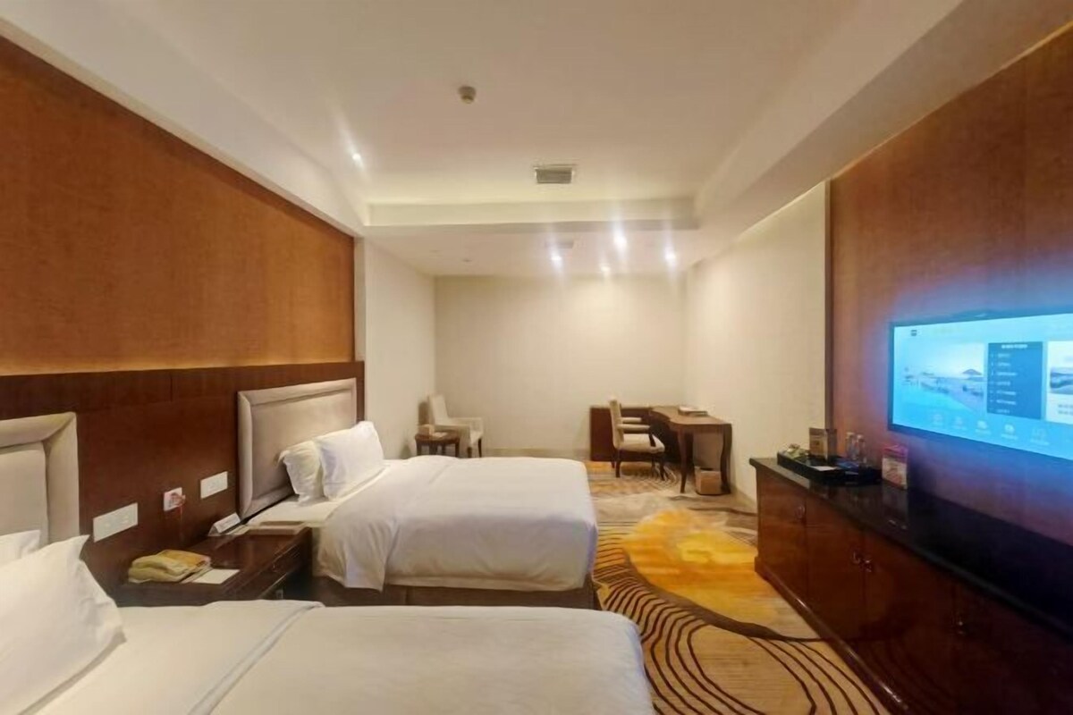 A hotel room with two beds, a desk, a chair, a television, and a carpeted floor.