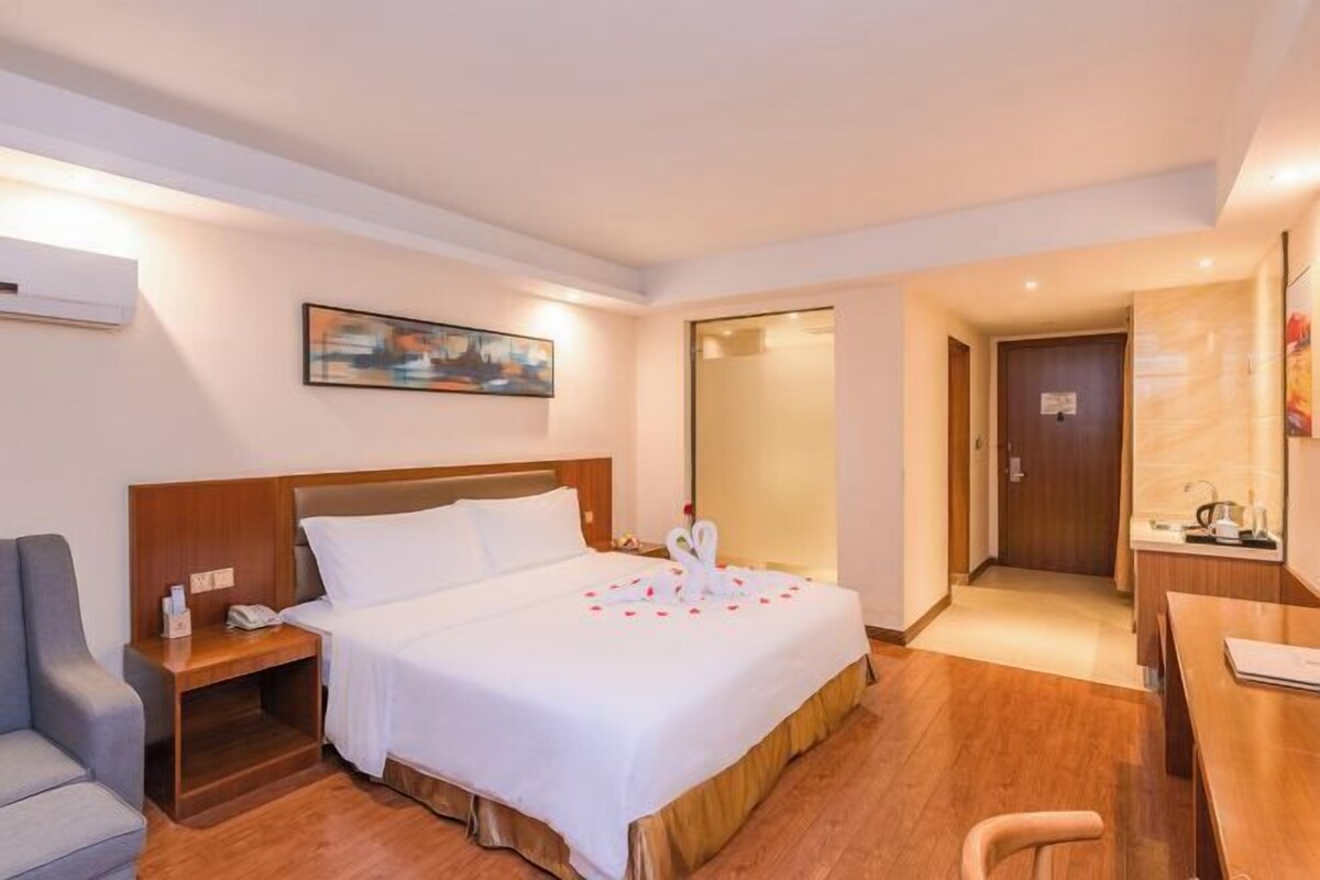 A hotel room with a bed, a desk, a chair, a nightstand, and a painting on the wall.