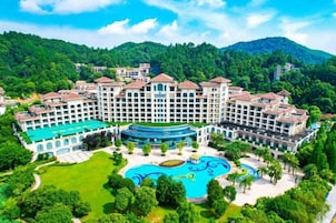 Un hotel grande con varias construcciones, una piscina central y vegetación circundante.