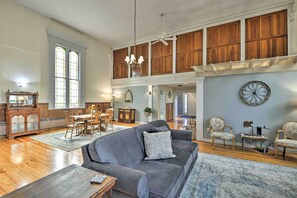 Een ruime woonkamer met een hoge plafond, houten lambrisering, een eethoek en een groot raam.