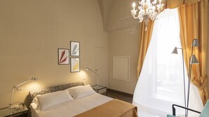Een hotelkamer met een bed, een bureau met lamp, een stoel, een kroonluchter en kunst aan de muur.