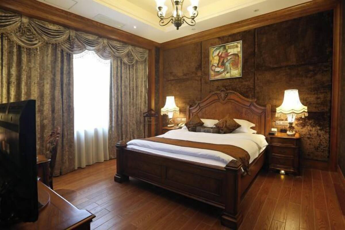 A large bed with a wooden headboard, two bedside lamps, a television, and a painting on the wall.