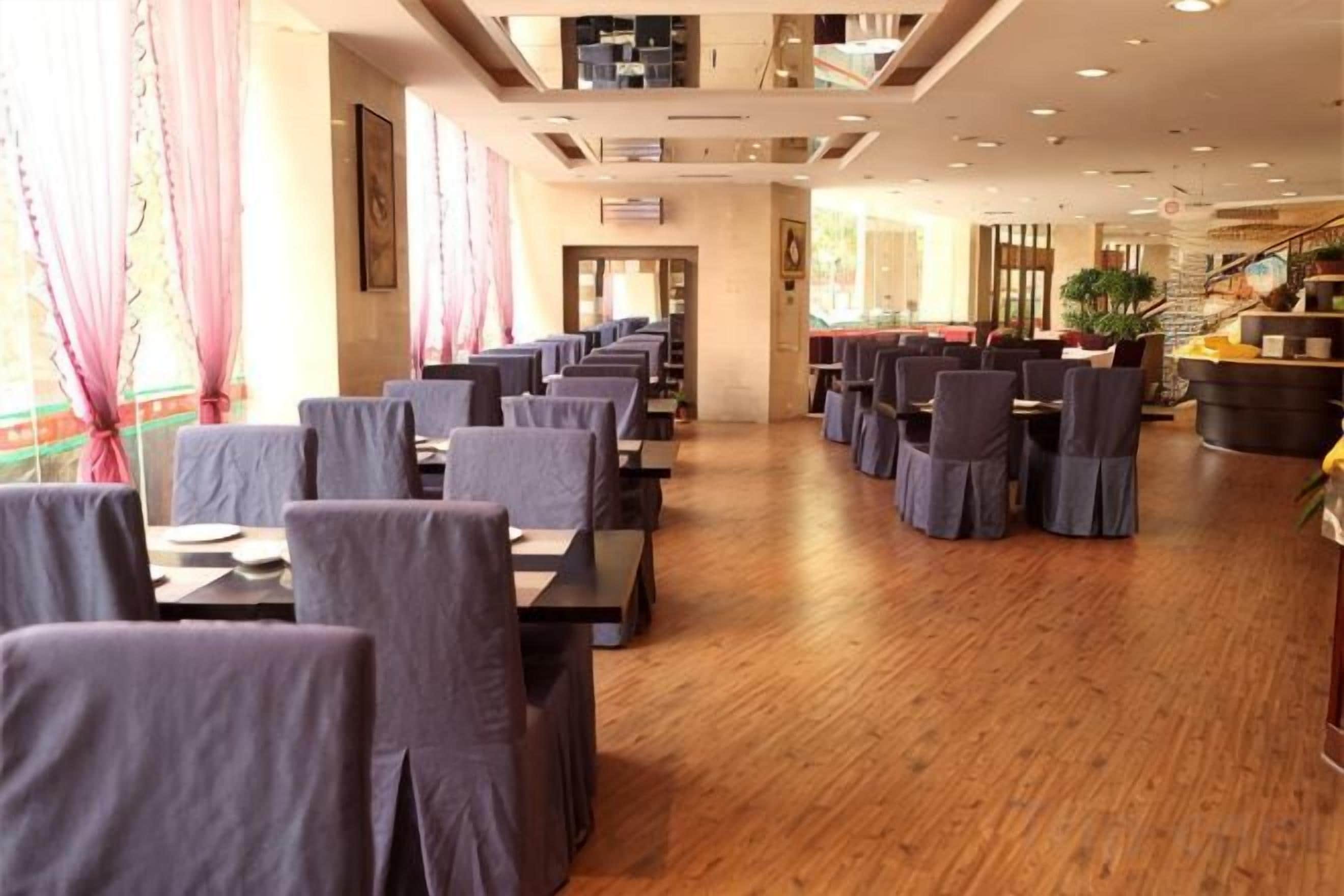 A restaurant with rows of tables and chairs, wooden flooring, and a staircase in the background.