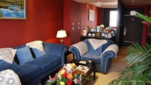 A hotel room with two blue sofas, a coffee table with flowers, a painting on the wall, and a minibar. - Minghao Hotel (Chongqing)