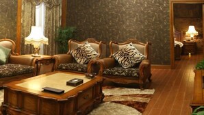 A traditional living room with a wooden coffee table, two armchairs with patterned cushions, a sofa, a lamp, and a patterned rug. - Minghao Hotel (Chongqing)