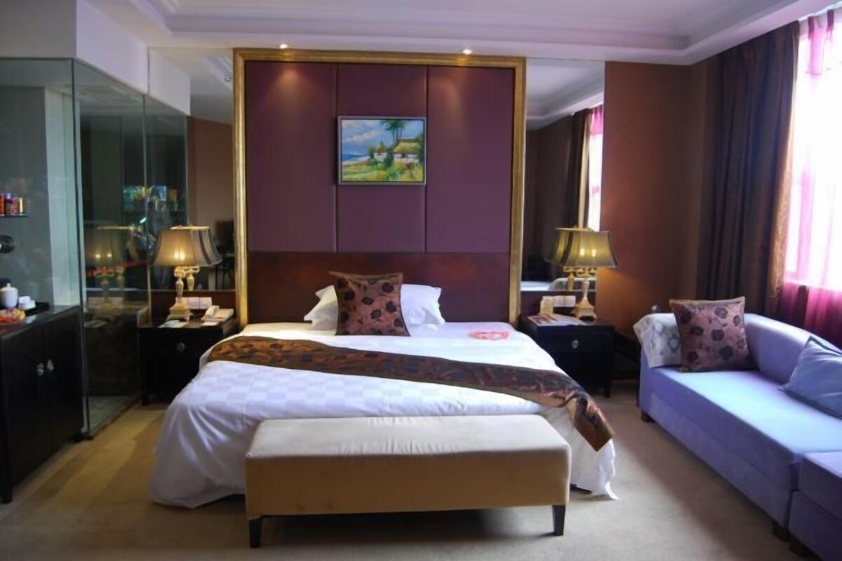 A hotel room with a large bed, a sofa, a desk, and a glass cabinet.