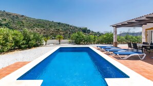 A rectangular swimming pool with blue tiles, surrounded by a patio area with lounge chairs and a table. - Holiday Home "Verdejo" with Mountain Views, Pool, and Wi-Fi (Cómpeta)