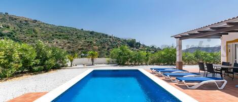 Ein rechteckiger Pool mit blauen Fliesen, umgeben von einer Terrassenanlage mit Liegestühlen und einem Tisch.