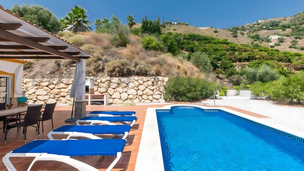 Ein Pool mit Liegestühlen, einer Pergola und einer Steinmauer.