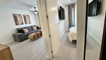 Un dormitorio moderno con una cama, un sofá gris y un televisor montado en la pared.