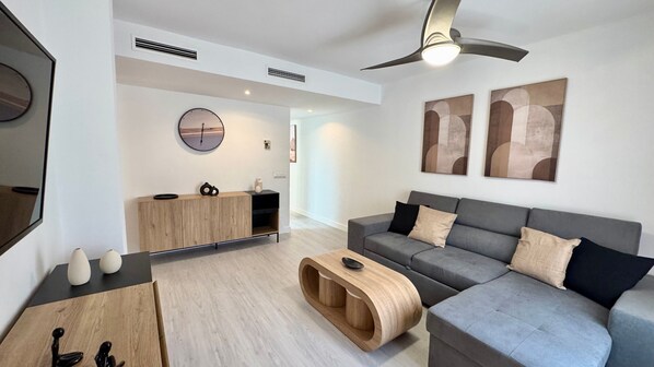 Un salon moderne avec un canapé gris, une table d’appoint en bois et un ventilateur de plafond.