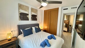 Un lit bien fait, avec des oreillers, une lampe de chevet et un ventilateur de plafond, dans une chambre d’hôtel.