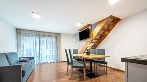 Ein modernes Wohnzimmer mit einer Holztreppe, einem Esstisch mit Stühlen, einer Couch und einer Küchenzeile.