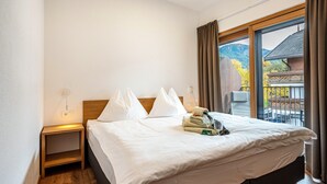 Ein Hotelzimmer mit Bett, Nachttisch, Fenster mit Vorhängen und Blick auf ein Gebäude und Bäume.