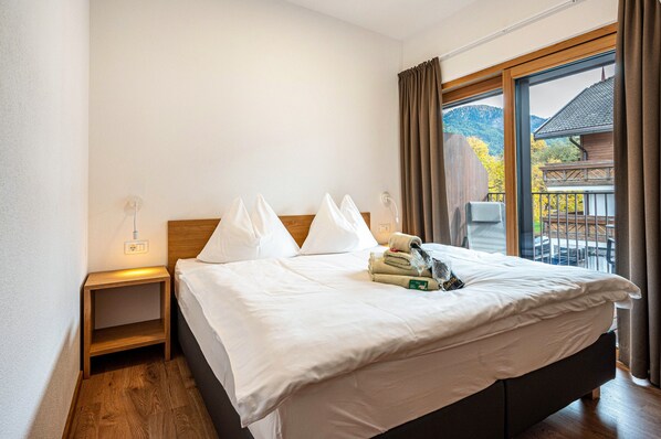 Une chambre d’hôtel avec un lit, une table de chevet, une fenêtre avec des rideaux et une vue sur un immeuble et des arbres.