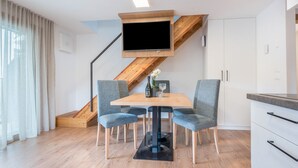 Un comedor moderno con una mesa, cuatro sillas, un televisor montado en una viga de madera y una escalera.