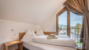 Un dormitorio con cama, mesita de noche, ventana con vista a un pueblo y balcón.