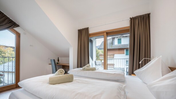 Habitación de hotel con dos camas, un escritorio y un amplio ventanal con cortinas.