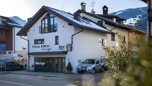Un edificio llamado 'Villa Colli Lounge' de estilo arquitectónico moderno, con un coche estacionado al frente y un paisaje montañoso de fondo.
