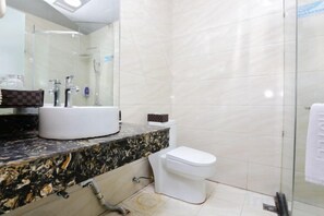 Un baño con encimera de mármol, un lavabo blanco, inodoro y mampara de cristal para la ducha.