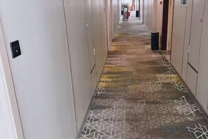 Un pasillo de hotel con piso estampado, taquillas a ambos lados y un bote de basura en el centro.