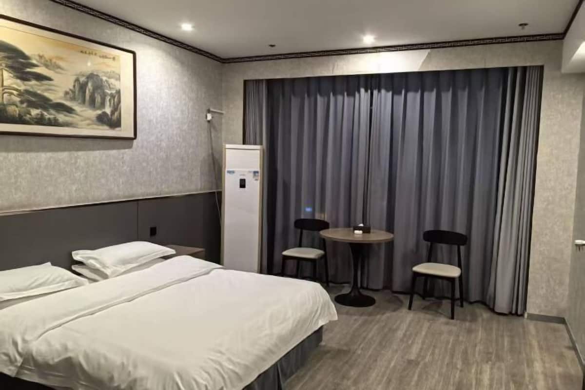 A hotel room with a bed, a desk, two chairs, a painting on the wall, and a curtain.