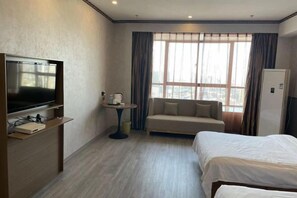 Habitación de hotel con cama, sofá, televisor, una mesita y ventana con cortinas.