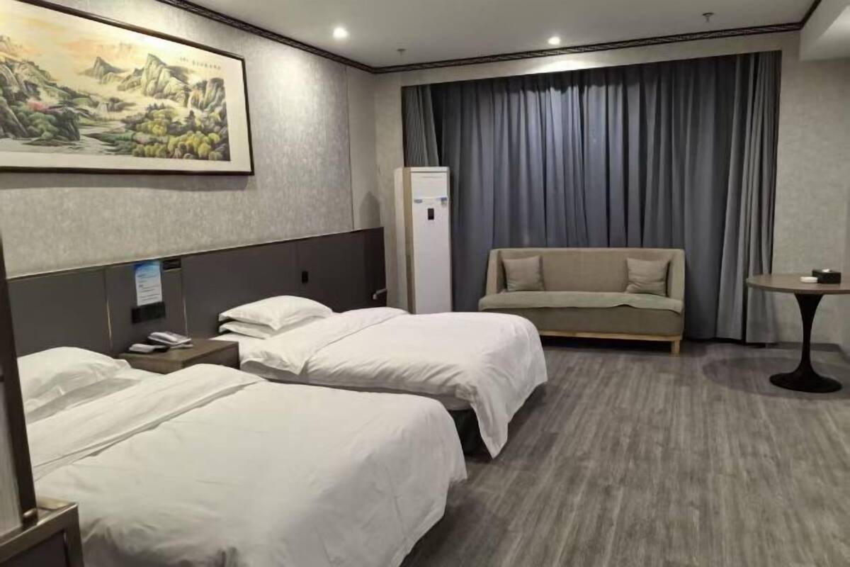 A hotel room with two beds, a sofa, a small table, a painting on the wall, and a refrigerator.