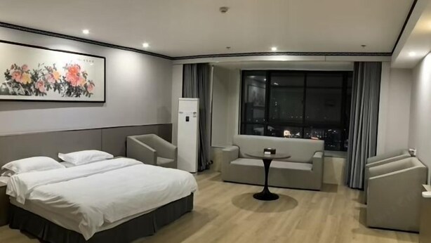 Habitación de hotel con cama, sofá, una mesita y un amplio ventanal con vista a la ciudad.