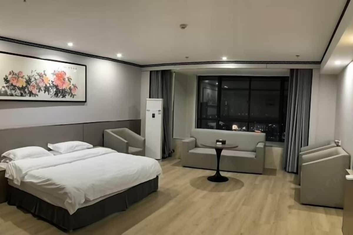 A hotel room with a bed, a sofa, a small table, and a large window with a city view.