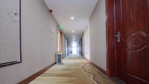 Un pasillo de hotel con suelo alfombrado, puertas de madera y una larga galería con una lámpara.