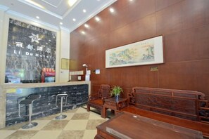 Zona de recepción de un hotel con mostrador de mármol, asientos de madera y una obra de arte enmarcada en la pared.