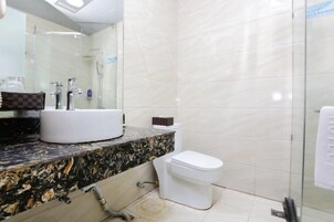 Un baño con encimera de mármol, un lavamanos blanco, inodoro y cabina de ducha con paredes de vidrio.