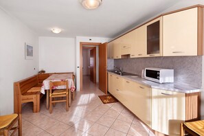 Cozinha compacta com micro-ondas, armários de madeira e área de refeições com banco e cadeiras.