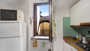 A compact kitchen with a built-in microwave, a window with a view of a building, a radiator, and a wooden countertop. - Apartment 'La Casa Tonda' (dolceacqua)