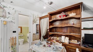 A dining area with a table set for four, a wooden bookshelf, and a television on a stand. - Apartment 'La Casa Tonda' (dolceacqua)