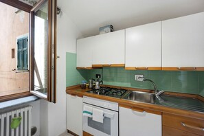 Eine kleine Küche mit Gaskochfeld, Spüle und einem Fenster mit Jalousien.
