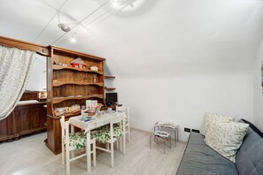 Ein gemütlicher Wohnraum mit Esstisch, Stühlen, einer Couch, einem Bücherregal und einem Fernseher.