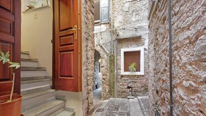 A narrow stone corridor with a wooden door, a potted plant, and a small window with a plant. - Apartment 'La Casa Tonda' (dolceacqua)