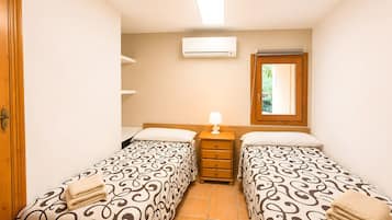 Une chambre avec deux lits simples, une table de chevet avec une lampe, un appareil de climatisation et une fenêtre donnant sur un paysage verdoyant.
