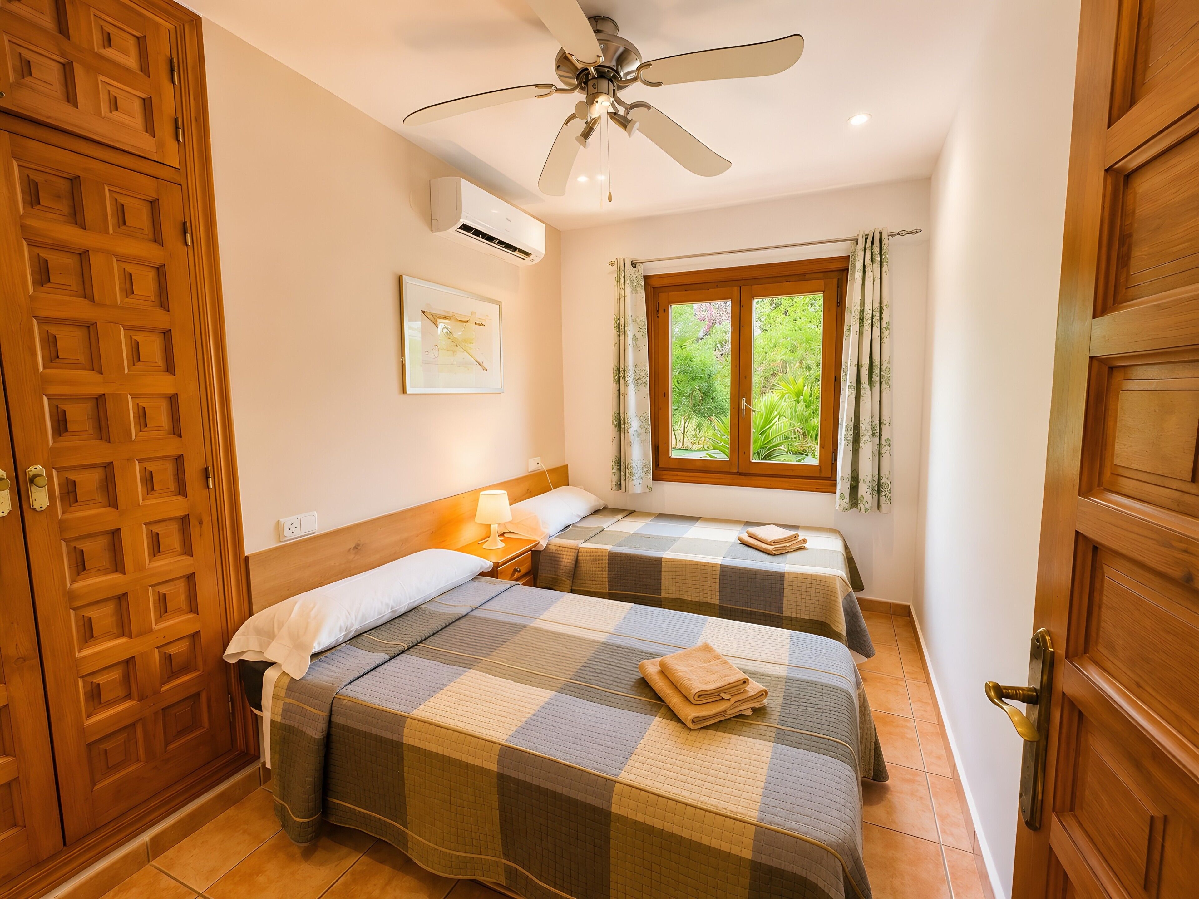 Una habitación con dos camas, ventilador de techo, aire acondicionado, ventana con cortinas y una puerta.