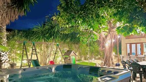 Un jacuzzi en un jardín con un conjunto de columpios, un comedor y un edificio al fondo.