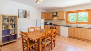 Una cocina moderna con armarios de madera, una mesa de comedor con sillas, un ventilador de techo y una ventana con vistas a la vegetación.