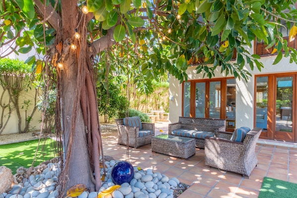An outdoor patio with wicker furniture, a large tree, and a decorative glass sphere.