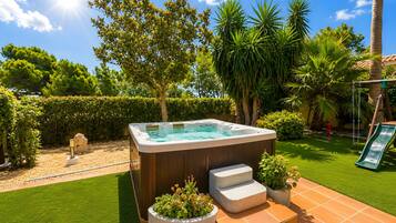 Un bain à remous entouré d’une pelouse bien entretenue, d’une terrasse en bois et de diverses plantes.